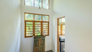 A room with a large window, a wooden cabinet, and a glimpse of a kitchen area. - Staymaster Bharini 2BR Villa Jet Pool (Nerul)