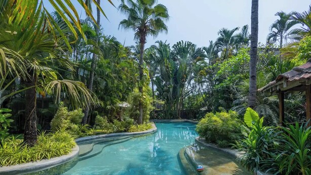 Une piscine entourée d’une végétation tropicale et d’une structure en bois.