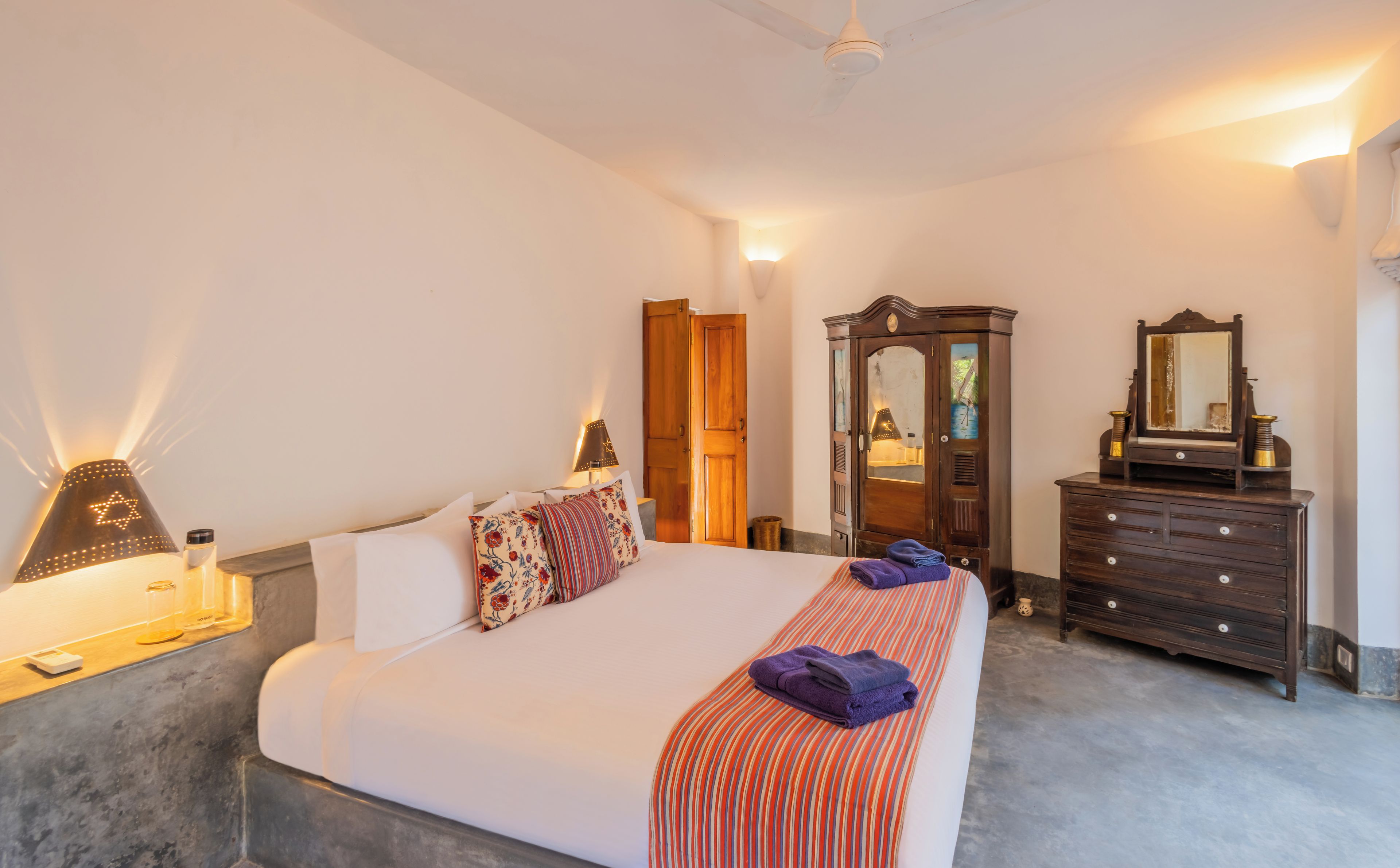 Un dormitorio con cama, lámparas de noche, cómoda, espejo y armario.