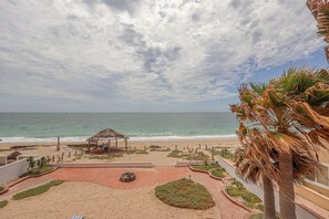 Une vue sur la plage avec une structure à toit de chaume, des palmiers et une promenade dallée.