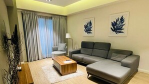 Ein modernes Wohnzimmer mit einem grauen Ecksofa, einem Holztisch, einer Stehlampe und zwei gerahmten Blätter-Kunstwerken an der Wand.