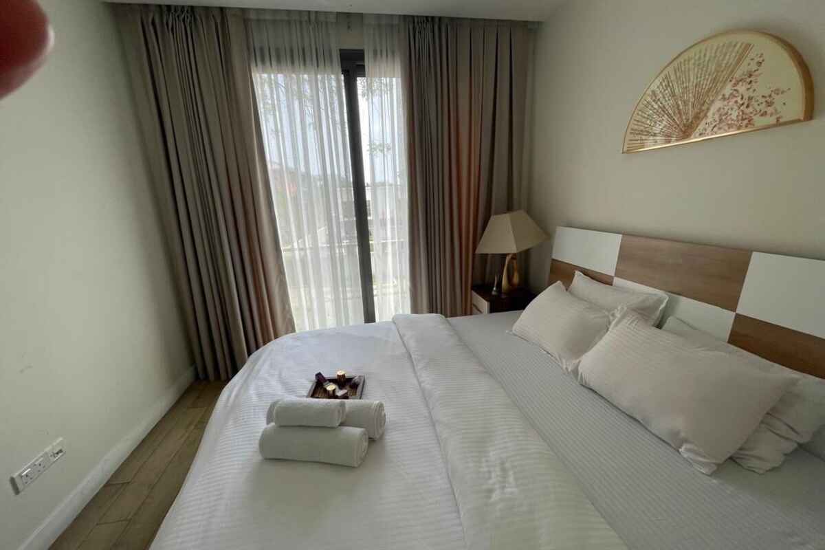 Ein Hotelzimmer mit einem großen Bett, einem Nachttisch mit einer Lampe und einem Fenster mit Vorhängen.