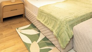 Ein aufgeräumtes Schlafzimmer mit einem Bett, zwei Nachttischen, einem Beistelltisch, einem grün gemusterten Teppich und einem Fenster mit Vorhängen.