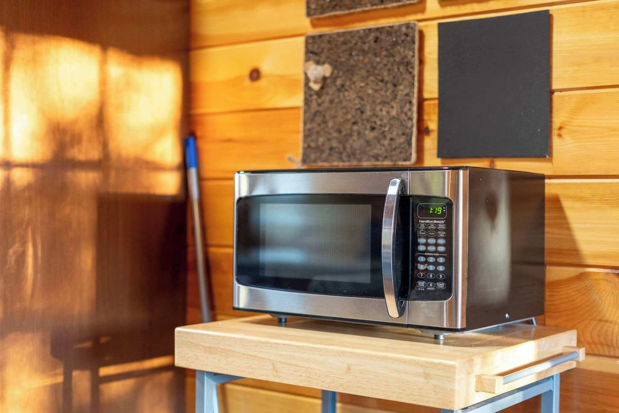 A stainless steel microwave on a wooden table in a room with wooden walls and a blackboard.
