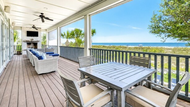 A covered outdoor deck with a seating area, a table, and a TV mounted on the wall. - 15 Dune Lane: Oceanfront Views Await, New Pool & Additions Coming Spring '27! (Hilton Head Island)