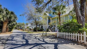 A residential street with a house featuring a front porch, a staircase, and a white picket fence. - 15 Dune Lane: Oceanfront Views Await, New Pool & Additions Coming Spring '27! (Hilton Head Island)