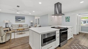 A modern kitchen with white cabinetry, a central island, stainless steel appliances, and a ceiling fan. - Renovated Home Close to Everything! Fenced Yard, Dogs Welcome! (Saint Simons Island)