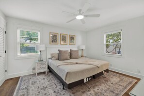 Un dormitorio con cama, mesitas de noche, ventilador de techo y obras de arte en las paredes.