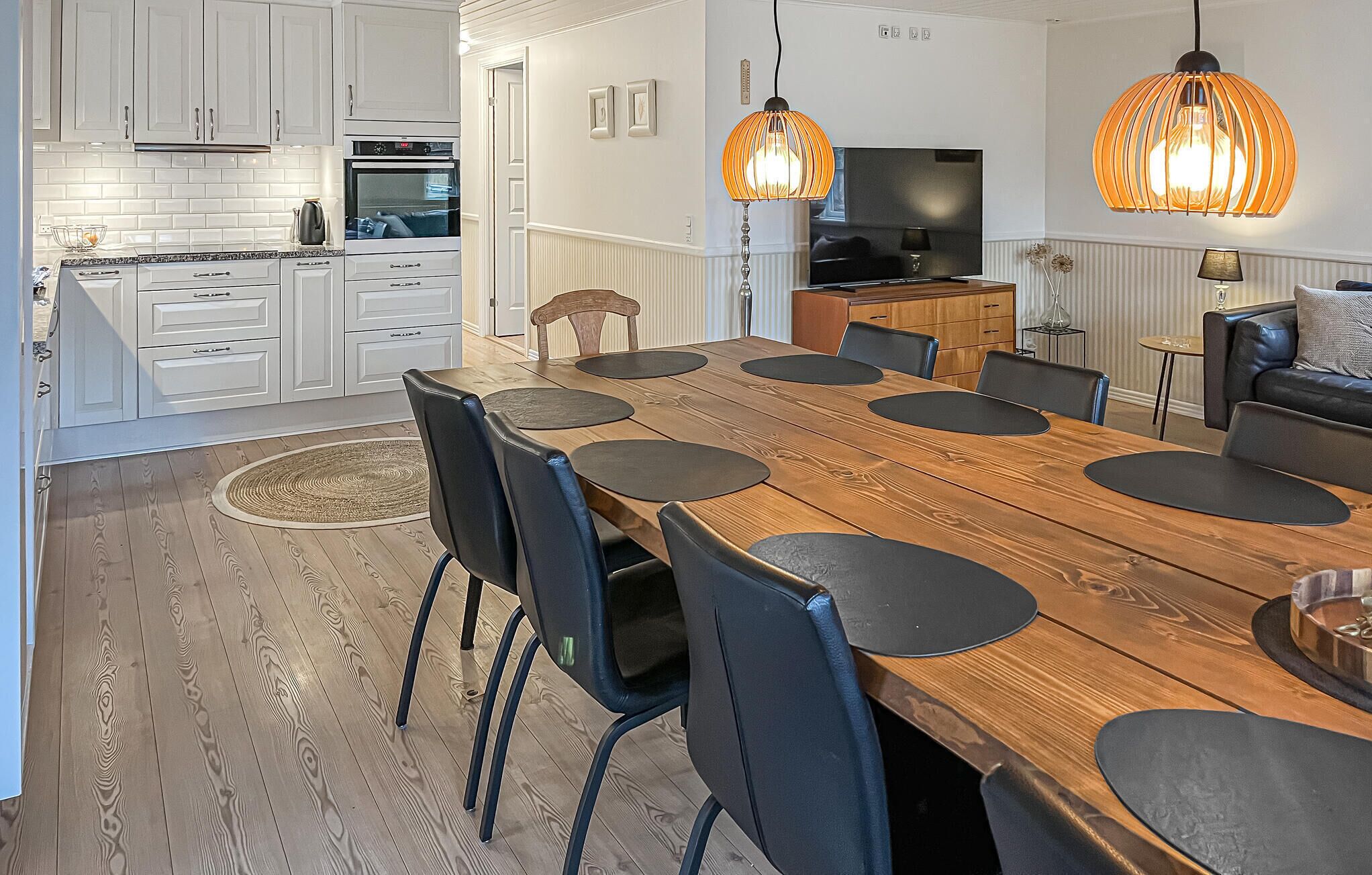 A modern kitchen with white cabinets, a built-in oven, and a dining area with a wooden table and black chairs.