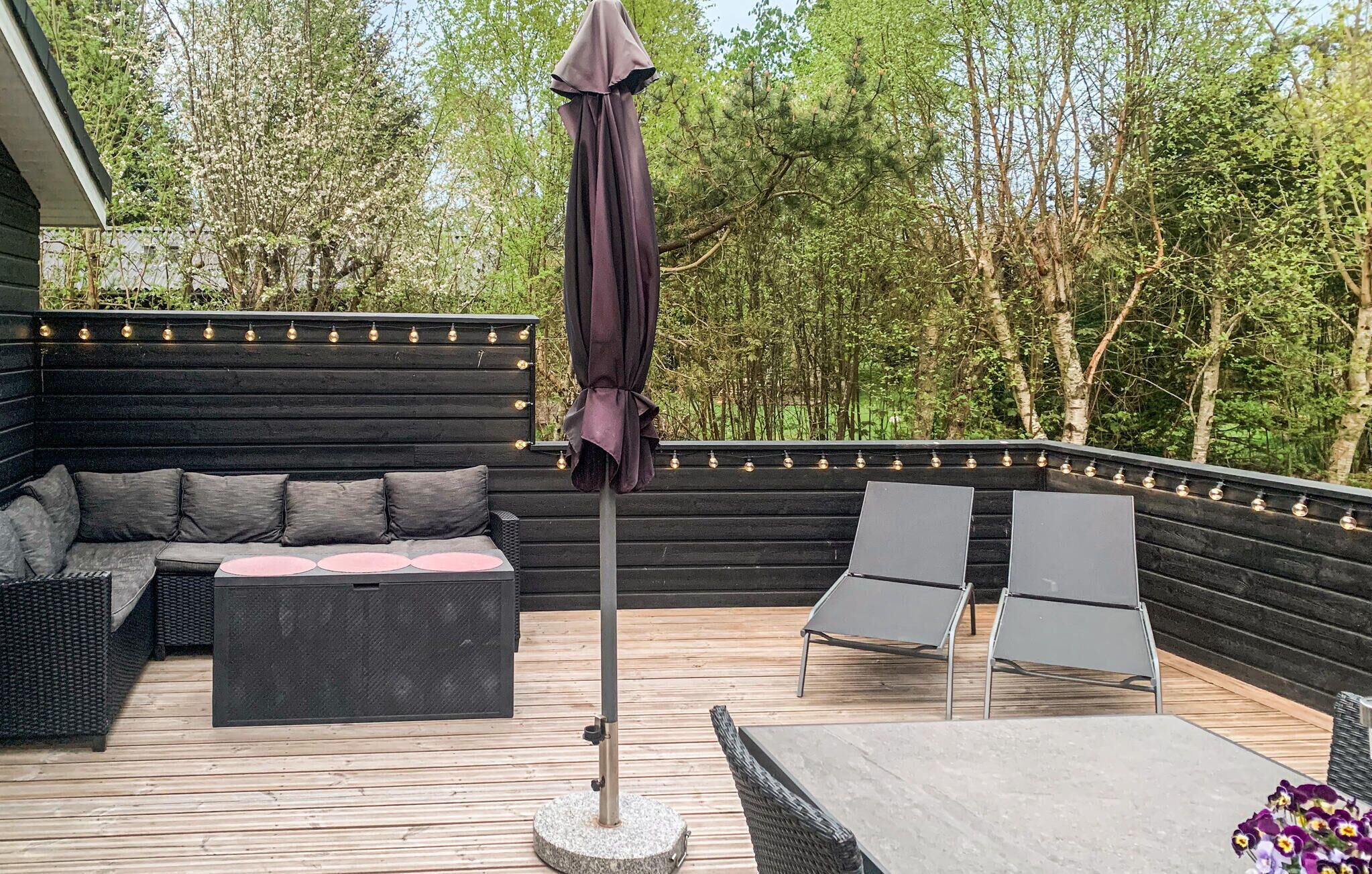 Eine Terrassenausstattung mit einer Couch, zwei Stühlen, einem Tisch und einer Pergola mit Beleuchtung.
