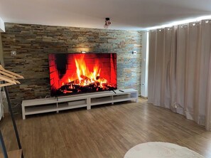 A living room with a fireplace, wooden flooring, and a white entertainment unit. - Renovated country house with swimming pool (L'Isle-sur-la-Sorgue)