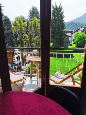 Ein Balkon mit Blick auf eine grüne Rasenfläche, Bäume und einen Berg. Holzstühle und ein Tisch sind vorhanden.