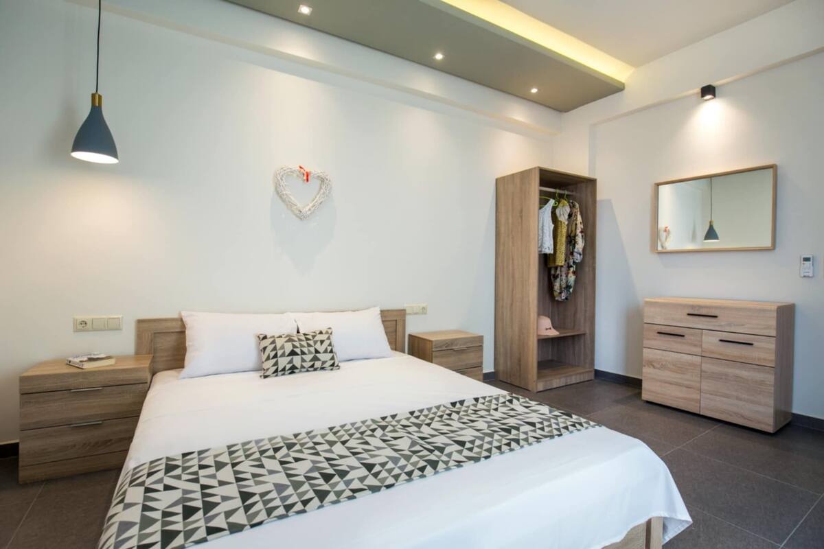 A modern bedroom with a bed, bedside tables, a wardrobe, a mirror, and a heart-shaped decoration on the wall.