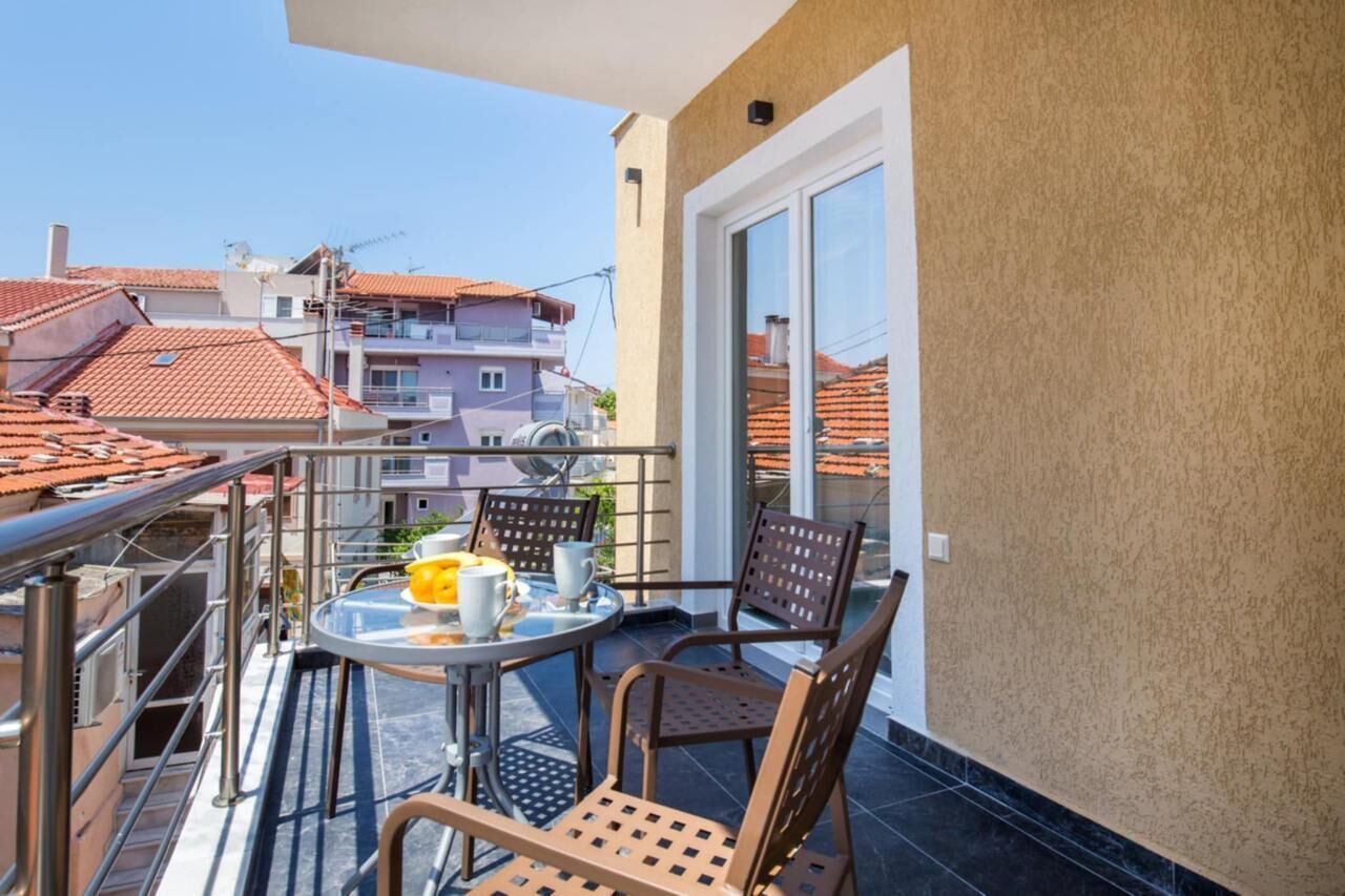 Un balcón con mesa y sillas, una puerta corrediza de vidrio y vistas a edificios cercanos.