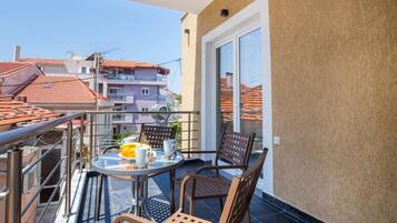 A balcony with a table and chairs, a sliding glass door, and a view of neighboring buildings.