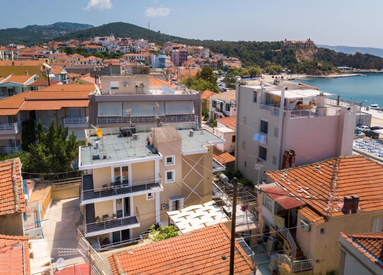 Une ville côtière aux bâtiments aux toits de tuiles rouges, avec un monument imposant situé sur une colline et un port de plaisance.