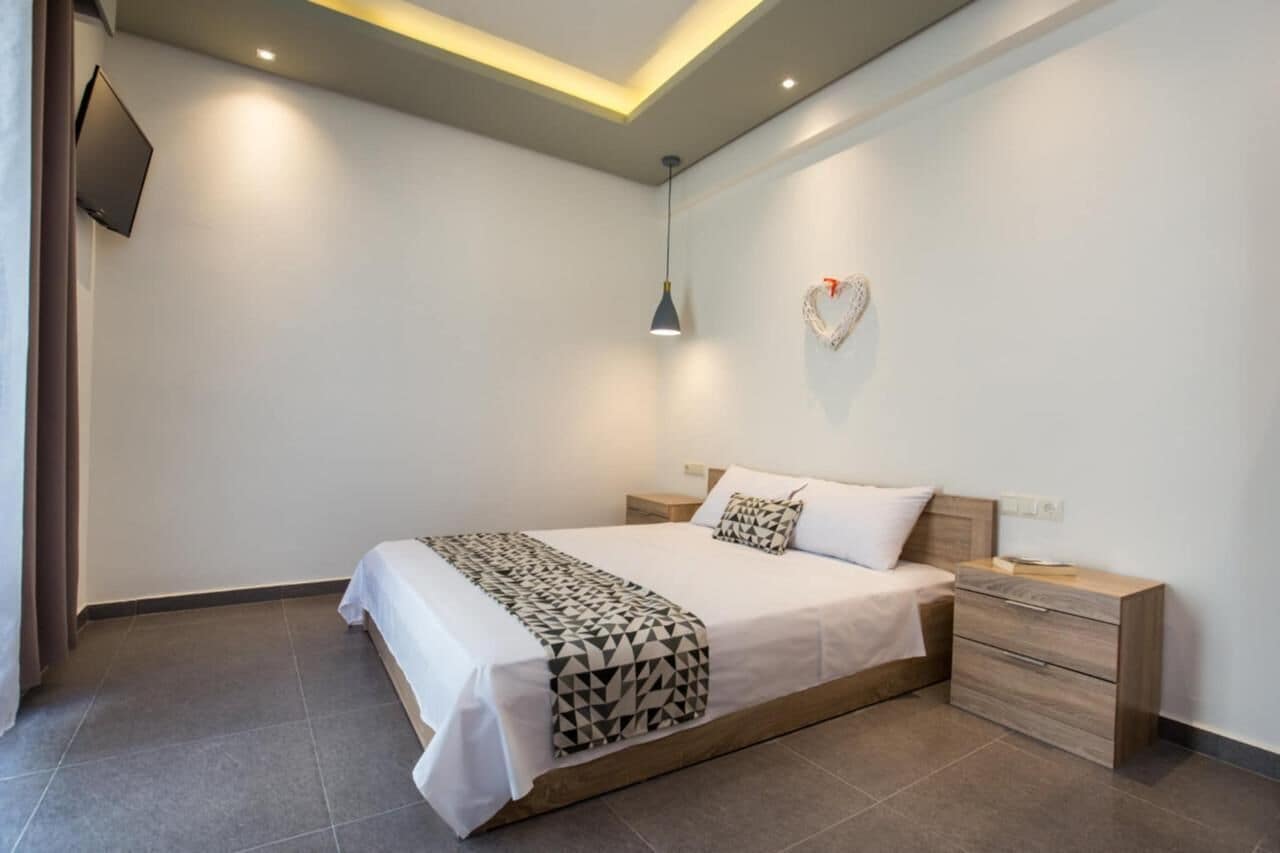 Un dormitorio moderno con cama, mesitas de noche, televisión y una decoración con forma de corazón en la pared.