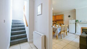 A staircase leading to a dining area with a table set for two, a kitchen with wooden cabinets, and a white radiator. - Superb 5 Bedroom TownHouse (Galway)