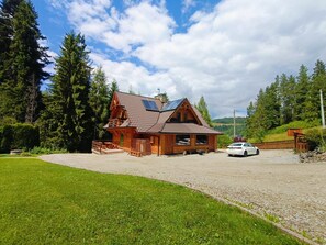 A wooden cabin with a sloped roof, a car parked in front, and a gravel driveway. - Apartment for 4 People With Garden View (Lapsze Nizne)