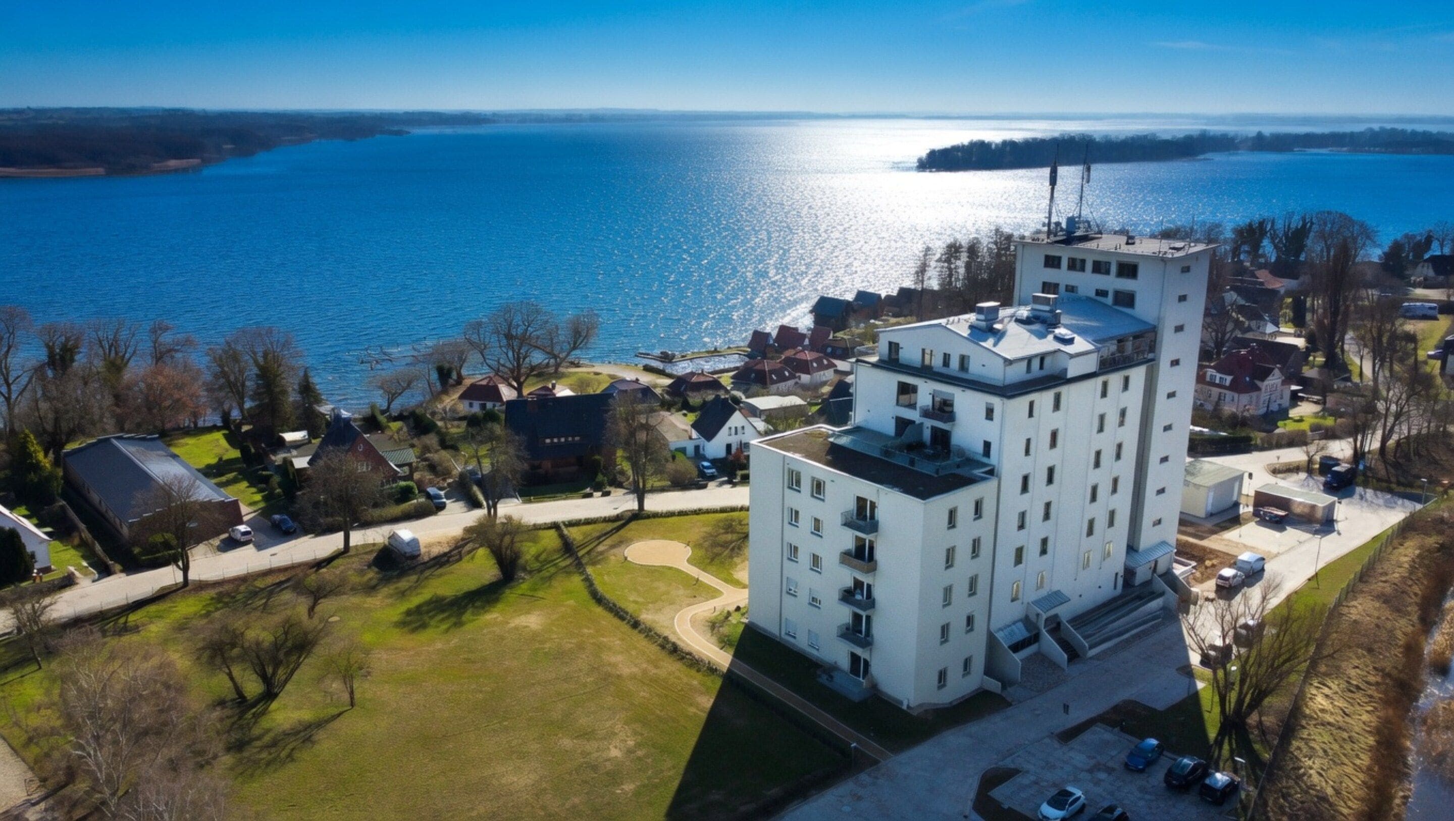 A high-rise building with multiple floors, surrounded by a residential area with houses and a large body of water in the background.