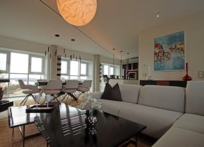 Ein modernes Wohnzimmer mit einer großen Couch, einem Essbereich mit Stühlen, einem Couchtisch und einem Bild an der Wand.