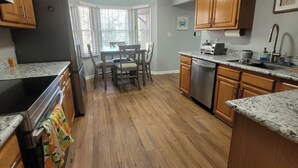A kitchen with wooden cabinets, a refrigerator, a dishwasher, a dining table with chairs, and a window with blinds. - Cozy home featuring a screened-in porch and access to a refreshing pool. Your oasis awaits!! (Ocean Pines)