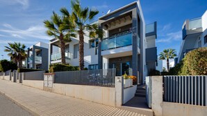 A modern multi-story building with balconies, palm trees, and a paved walkway. - Groundfloor Amay Punta Prima pool/sauna (Torrevieja)