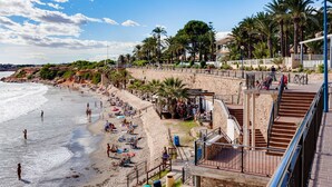 A beach with people, palm trees, and a staircase leading to a building. - Groundfloor Amay Punta Prima pool/sauna (Torrevieja)
