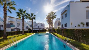 A swimming pool with two ladders, surrounded by palm trees and modern buildings. - Groundfloor Amay Punta Prima pool/sauna (Torrevieja)