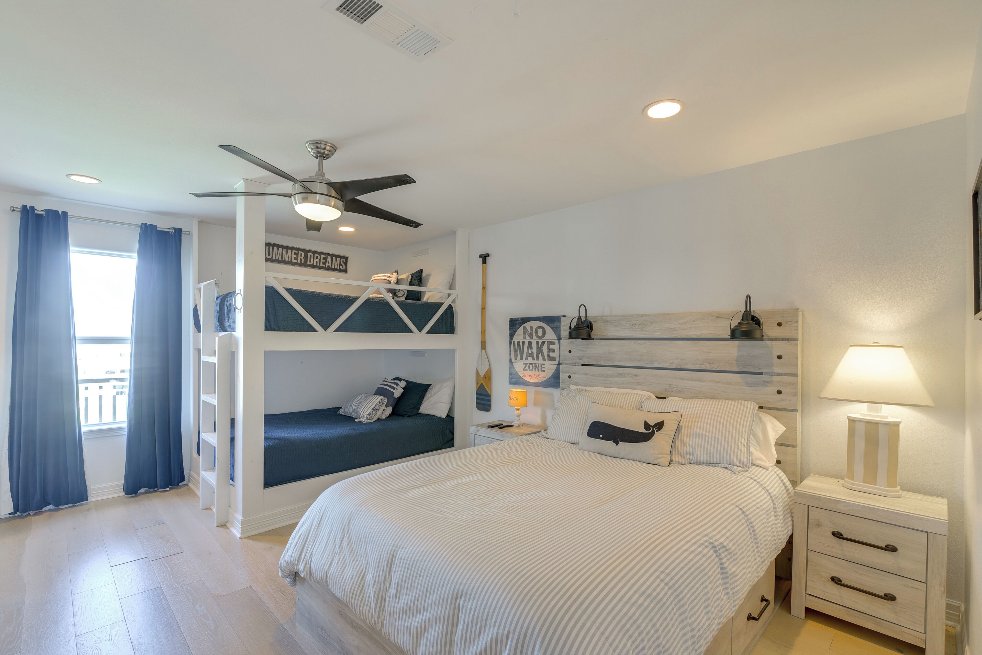 A bedroom with bunk beds, a ceiling fan, a nightstand with a lamp, and a sign on the wall.
