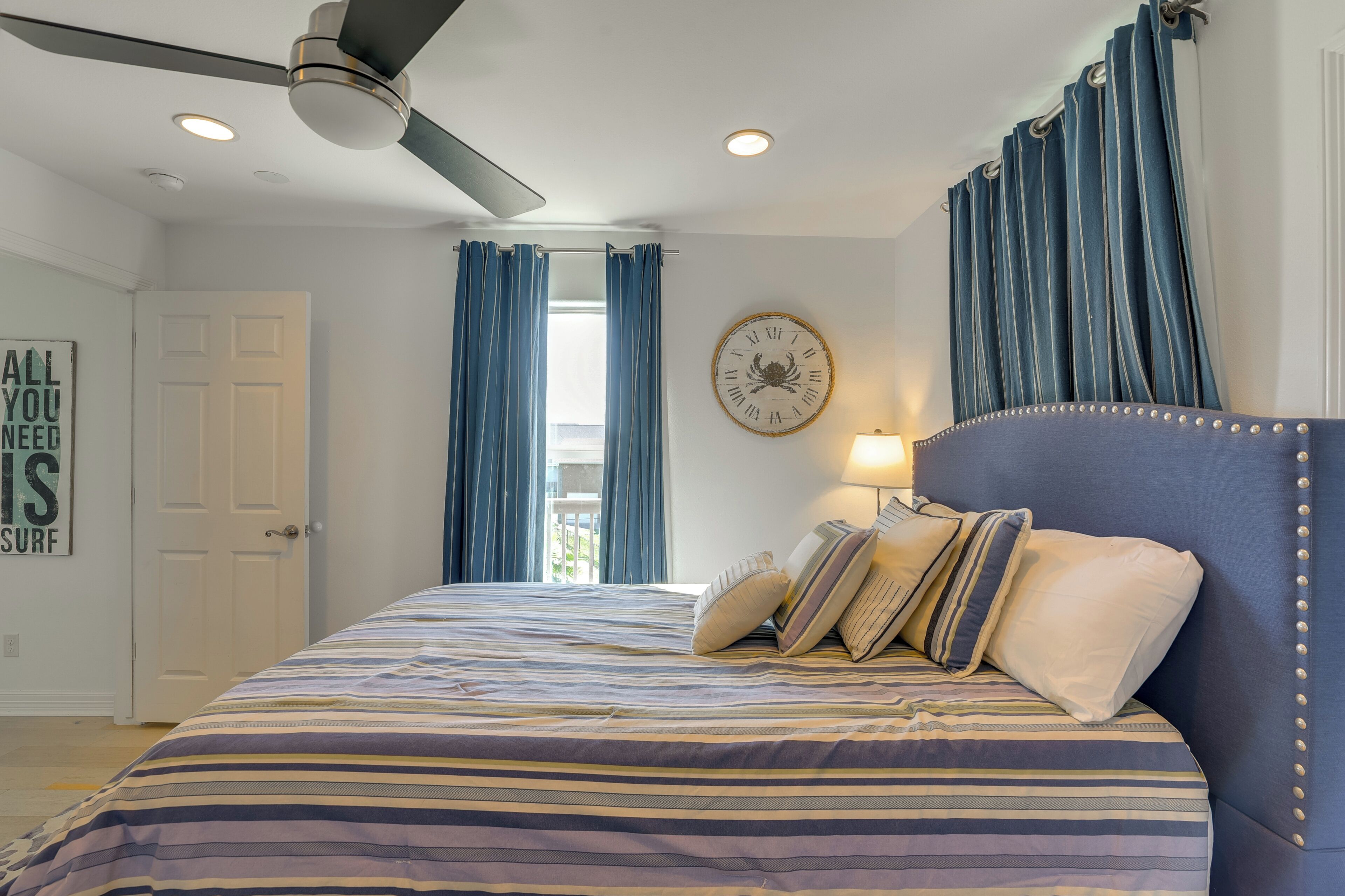 A bedroom with a bed, a ceiling fan, a clock, and curtains.