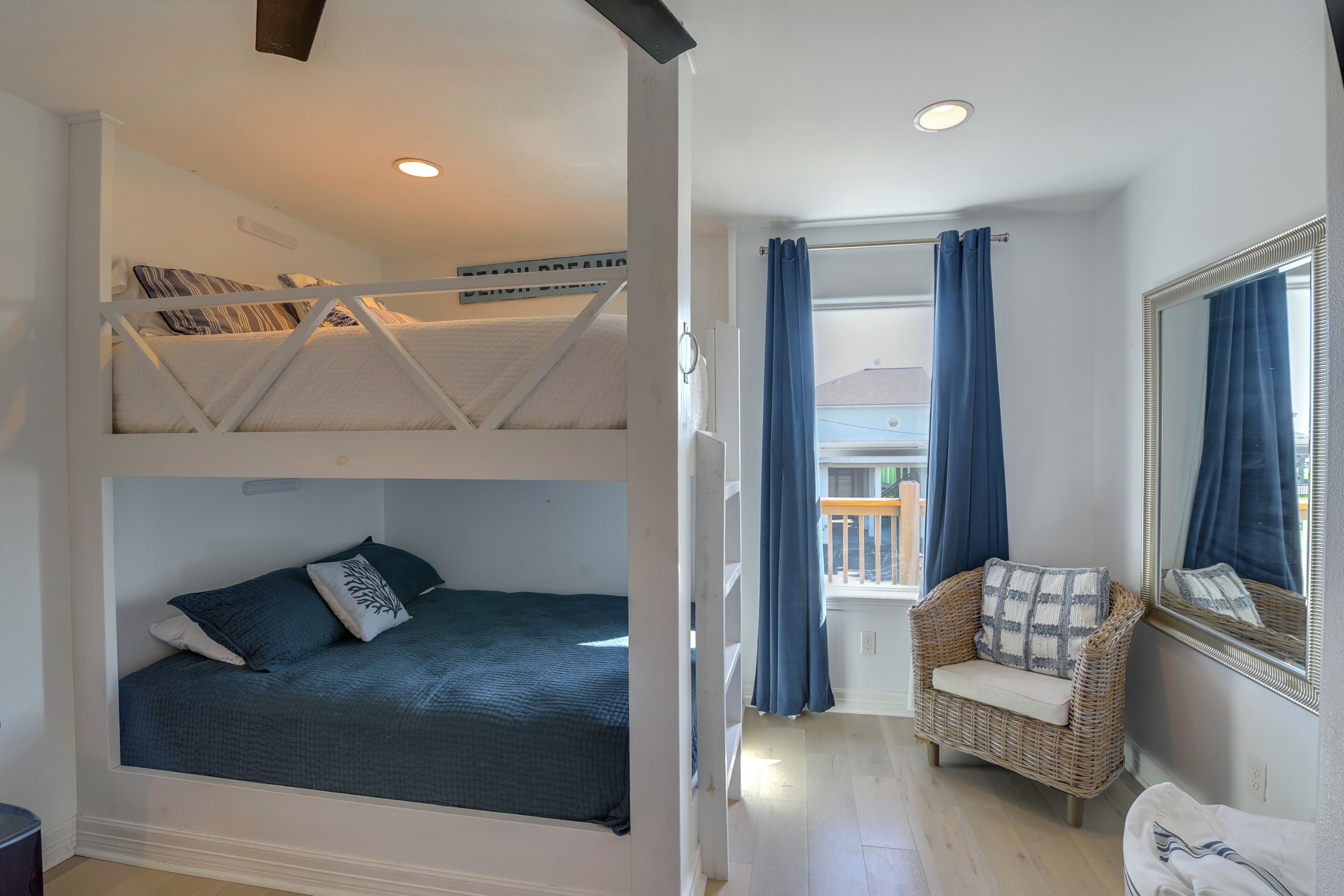 A room with bunk beds, a wicker chair, a mirror, and a view of the outside.