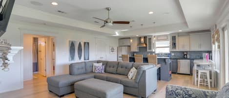 Amplia sala de estar con un sofá seccional gris, un sillón estampado y un comedor con una mesa pequeña y sillas.