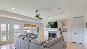 A spacious living room with a grey sectional sofa, a fireplace, a ceiling fan, and a TV mounted above it.