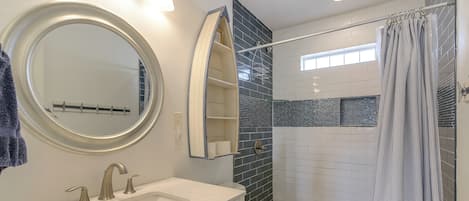 Een badkamer met een ronde spiegel, een wastafel, een toilet en een douche.