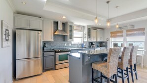 A modern kitchen with stainless steel appliances, a large island, and wicker bar stools.
