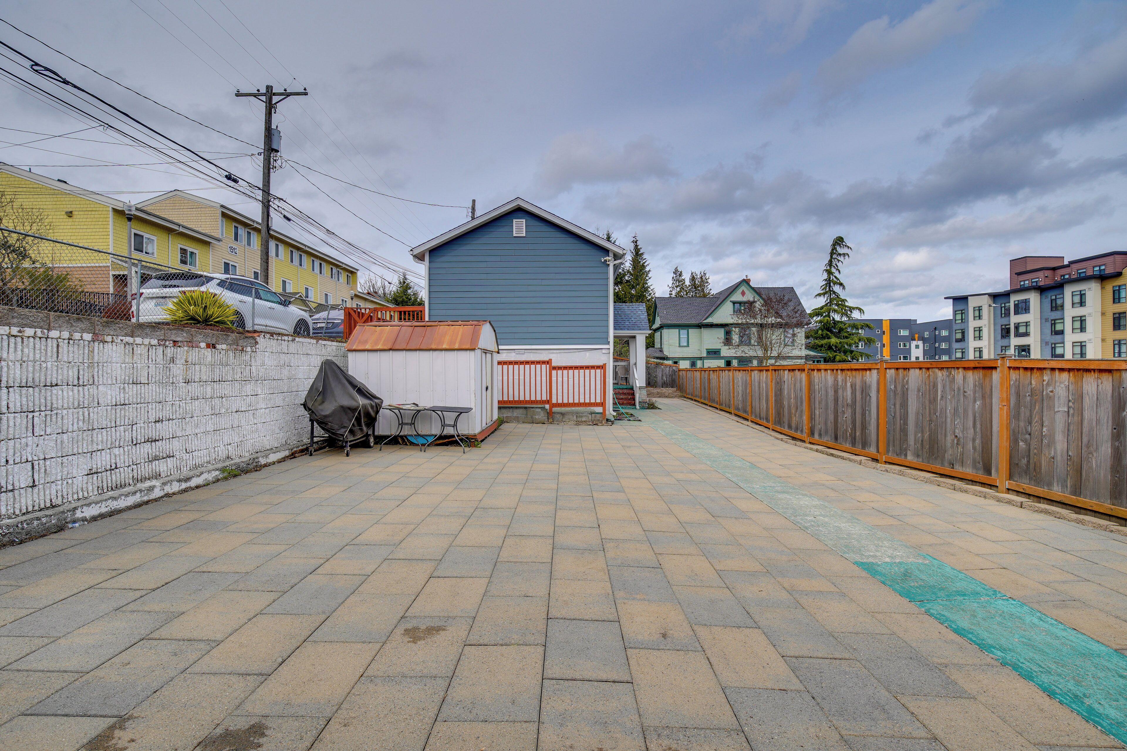 A paved backyard with a blue building, a white car, and a wooden fence.