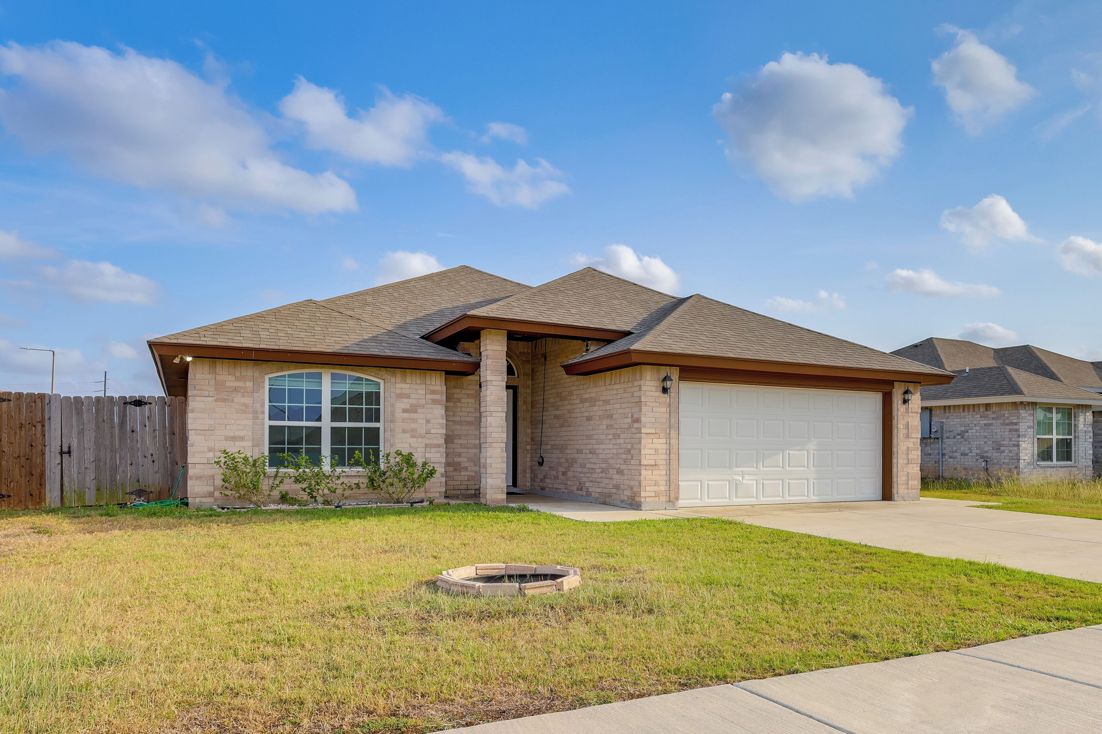 A two-story house with a garage, a front yard with a fire pit, and a wooden fence.