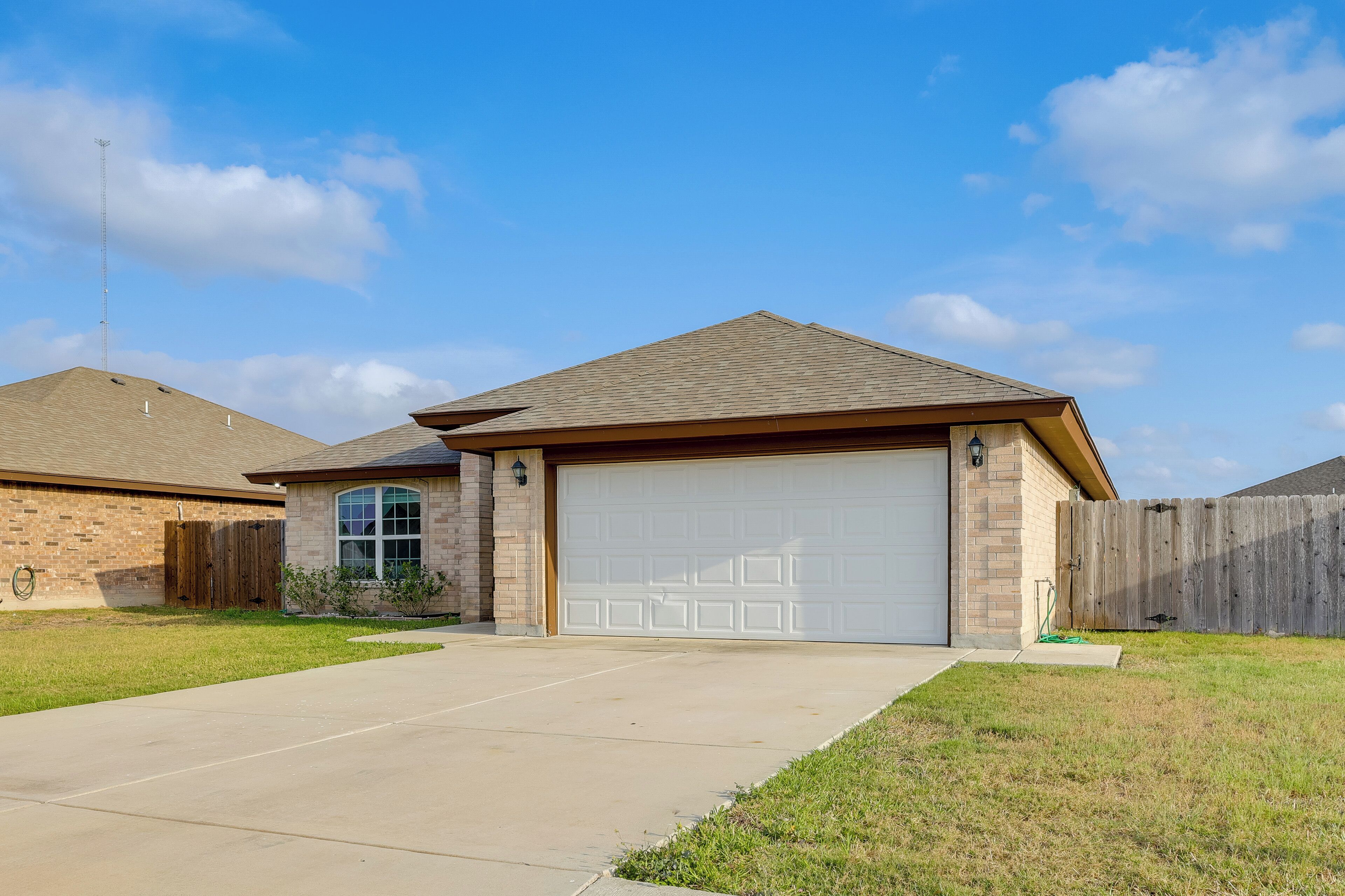 A residential house with a garage, a brick exterior, and a wooden fence.