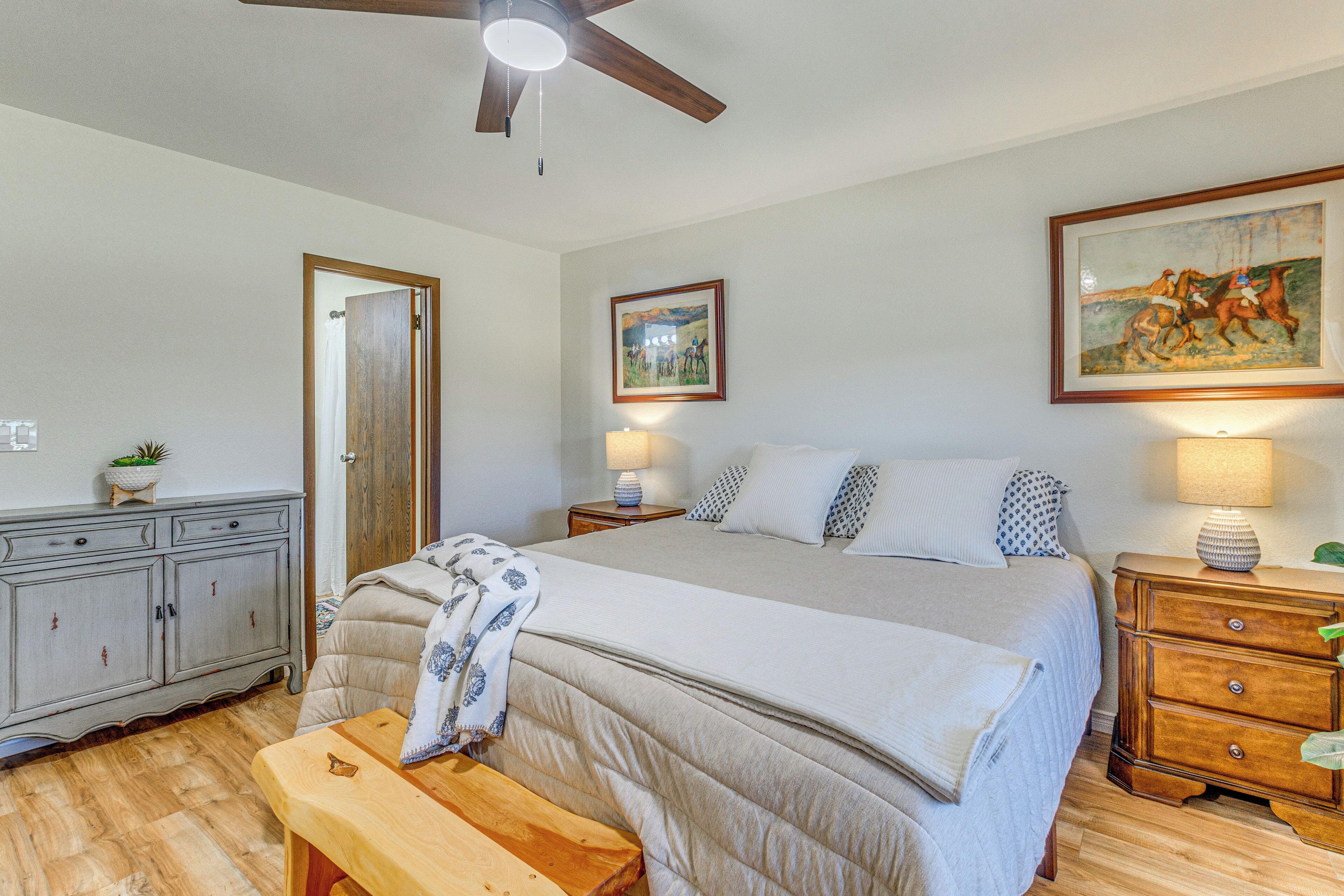 A bedroom with a bed, bedside tables, a ceiling fan, a door, a dresser, and a painting on the wall.