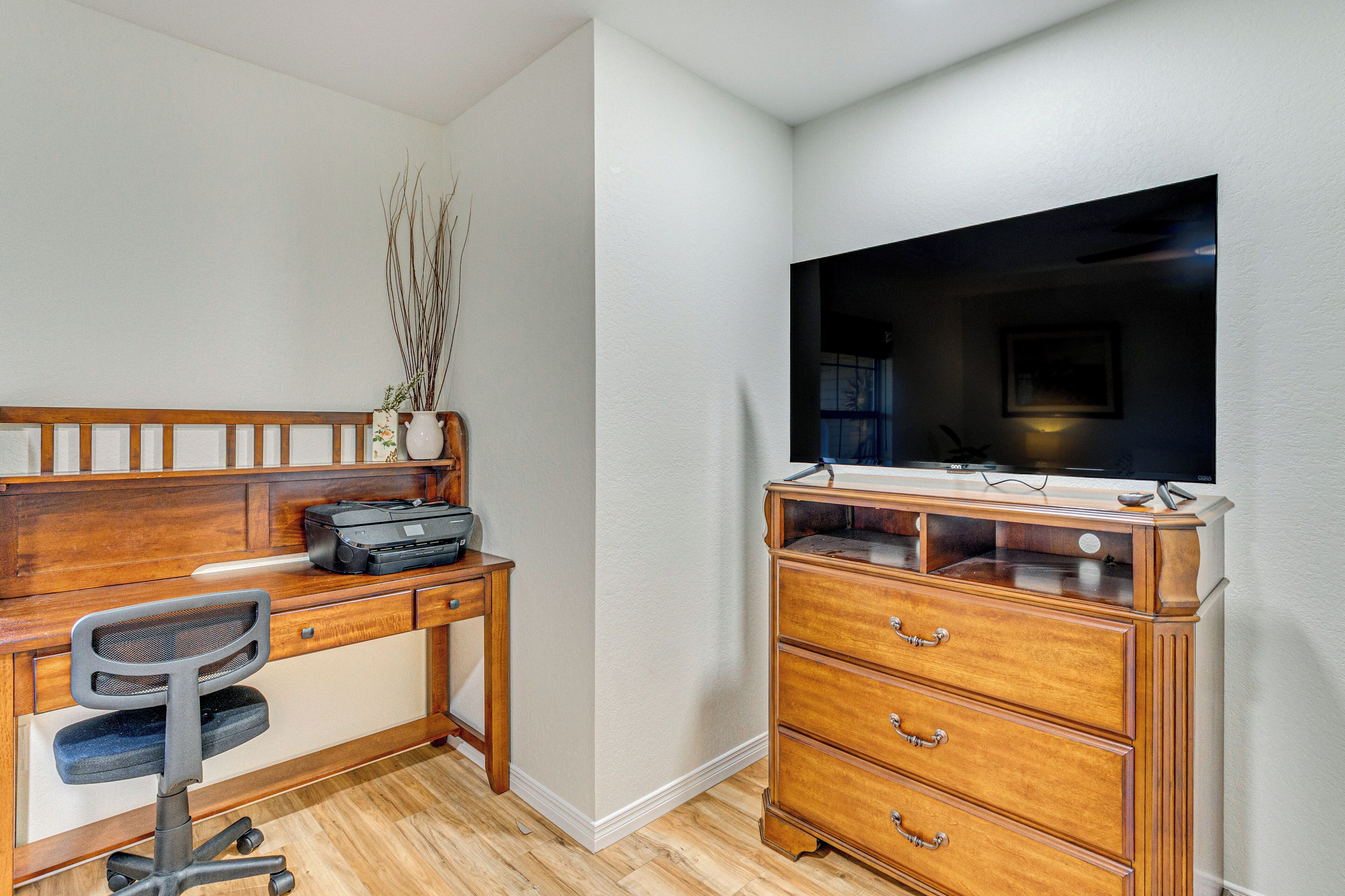 Quarto com escrivaninha de madeira, uma cadeira, cômoda e televisão.