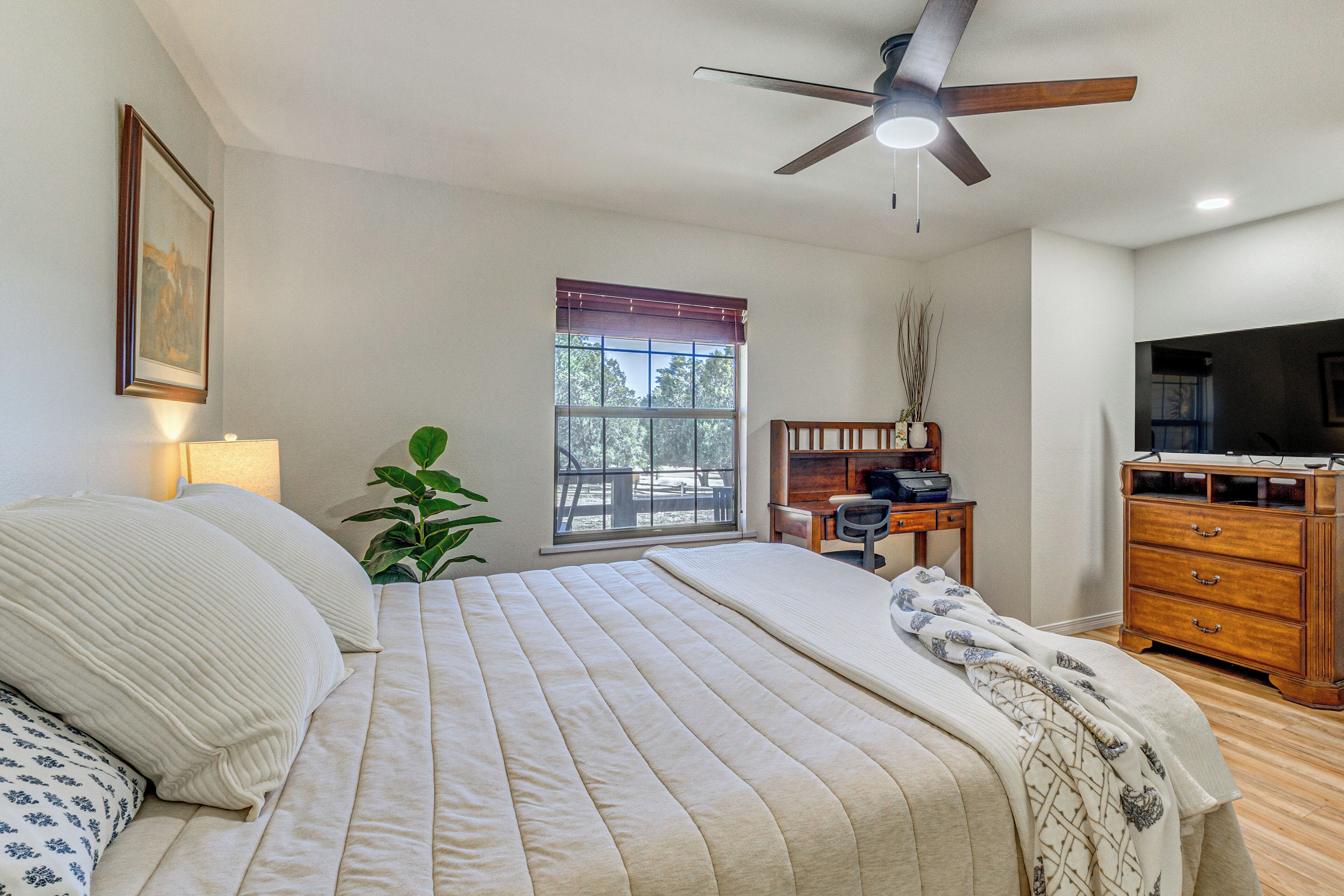 A bedroom with a bed, a desk, a television, and a ceiling fan.