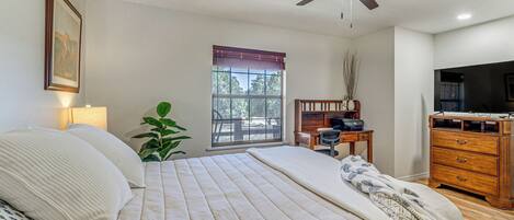 A bedroom with a bed, a desk, a television, and a ceiling fan.
