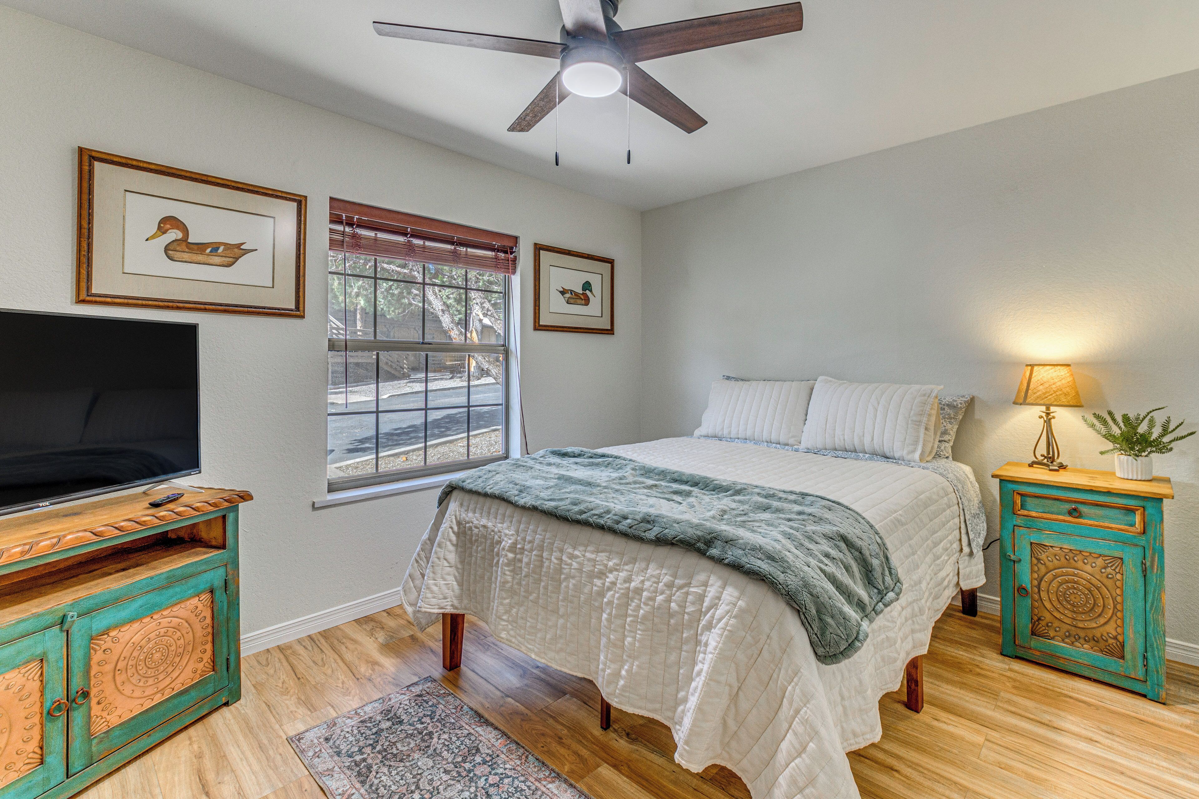 A bedroom with a bed, a TV, a ceiling fan, and a window with blinds.