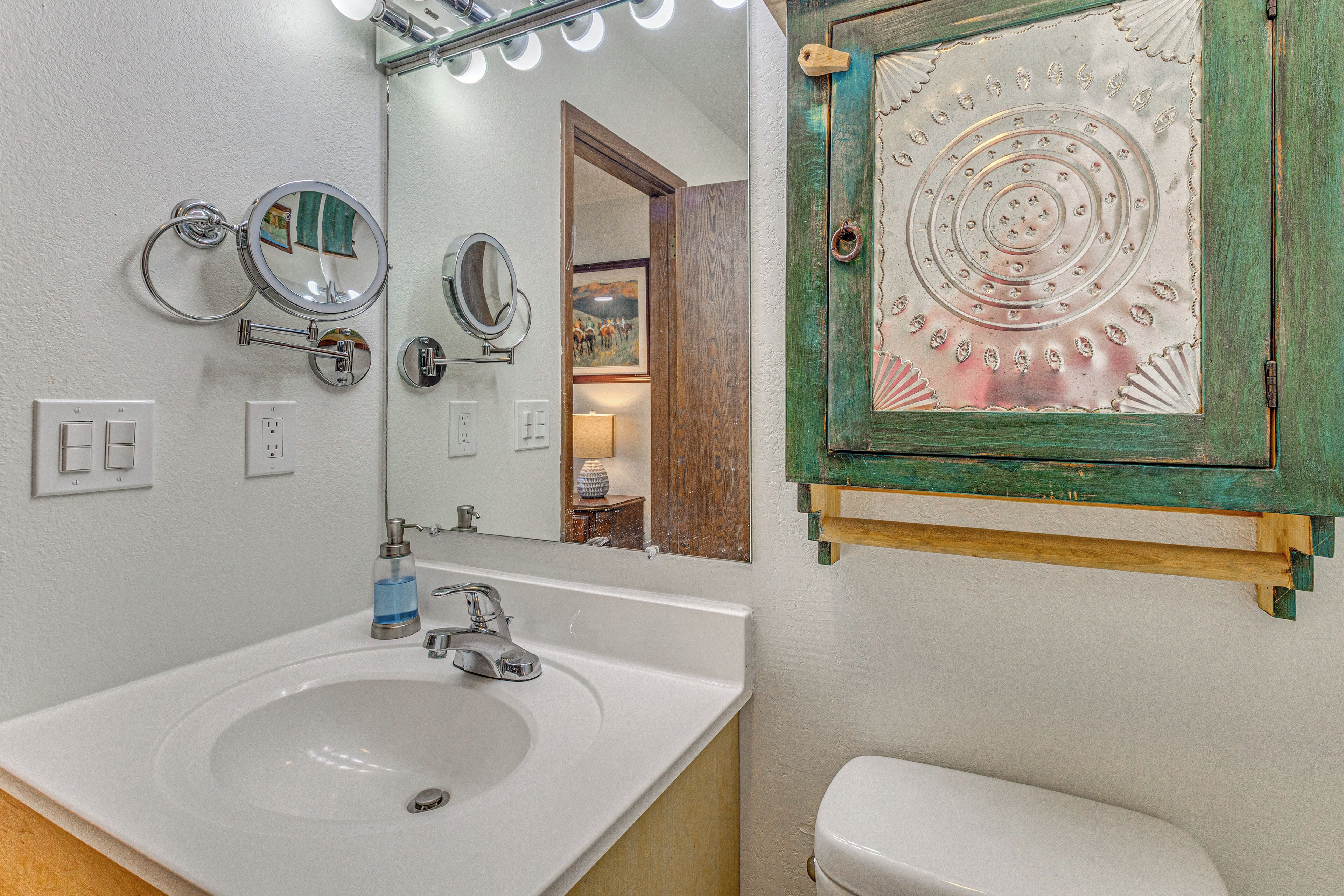 A bathroom with a sink, mirrors, a toilet, and a decorative metal plate.