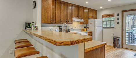 A kitchen with wooden cabinets, a central island with stools, a refrigerator, and a window.