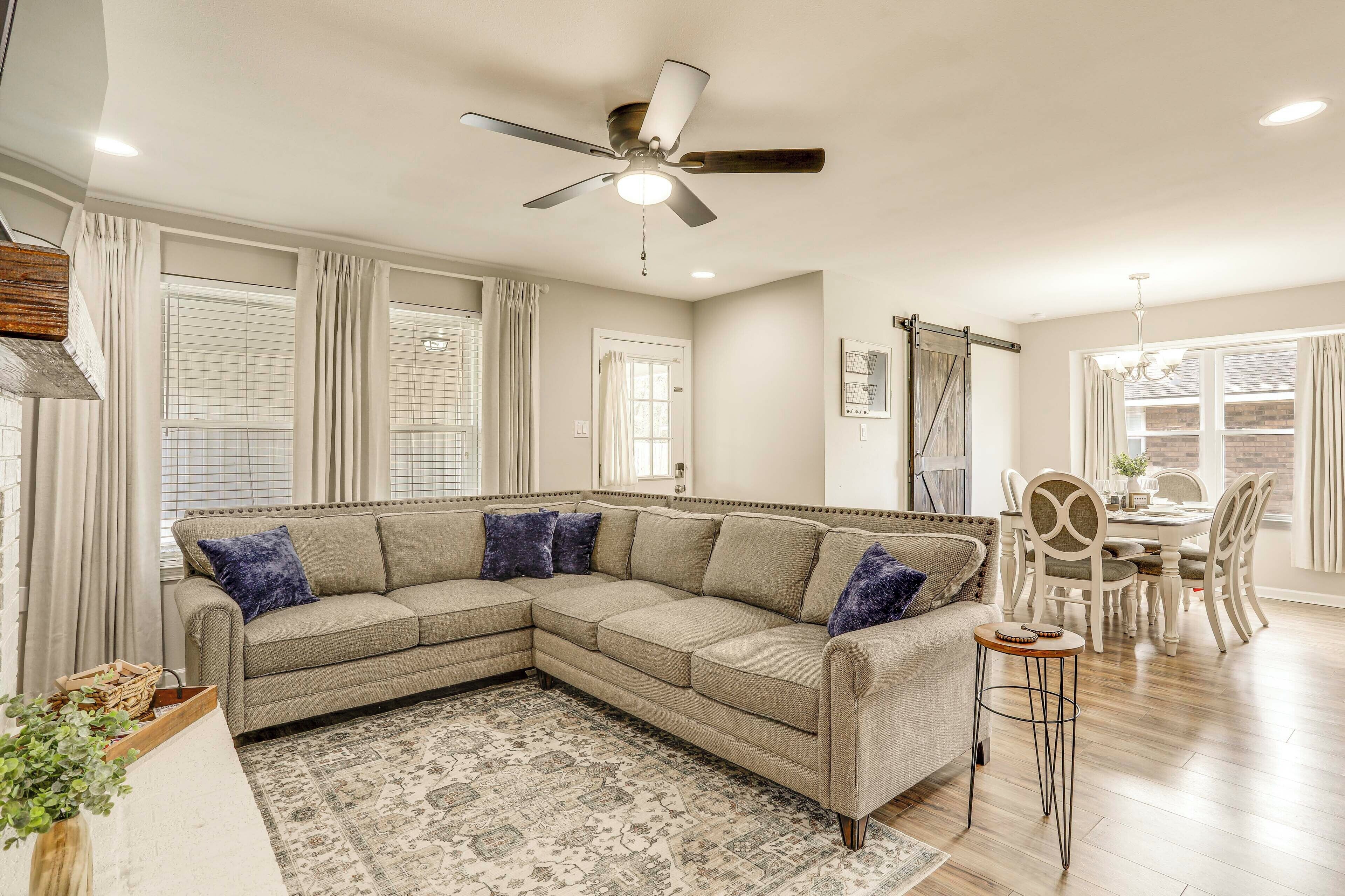 A living room with a sectional sofa, a dining area with a table and chairs, a ceiling fan, and a patterned rug.
