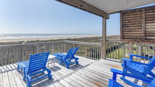 Eine Holzterrasse mit blauen Stühlen und einem Tisch mit Blick auf einen Strand.