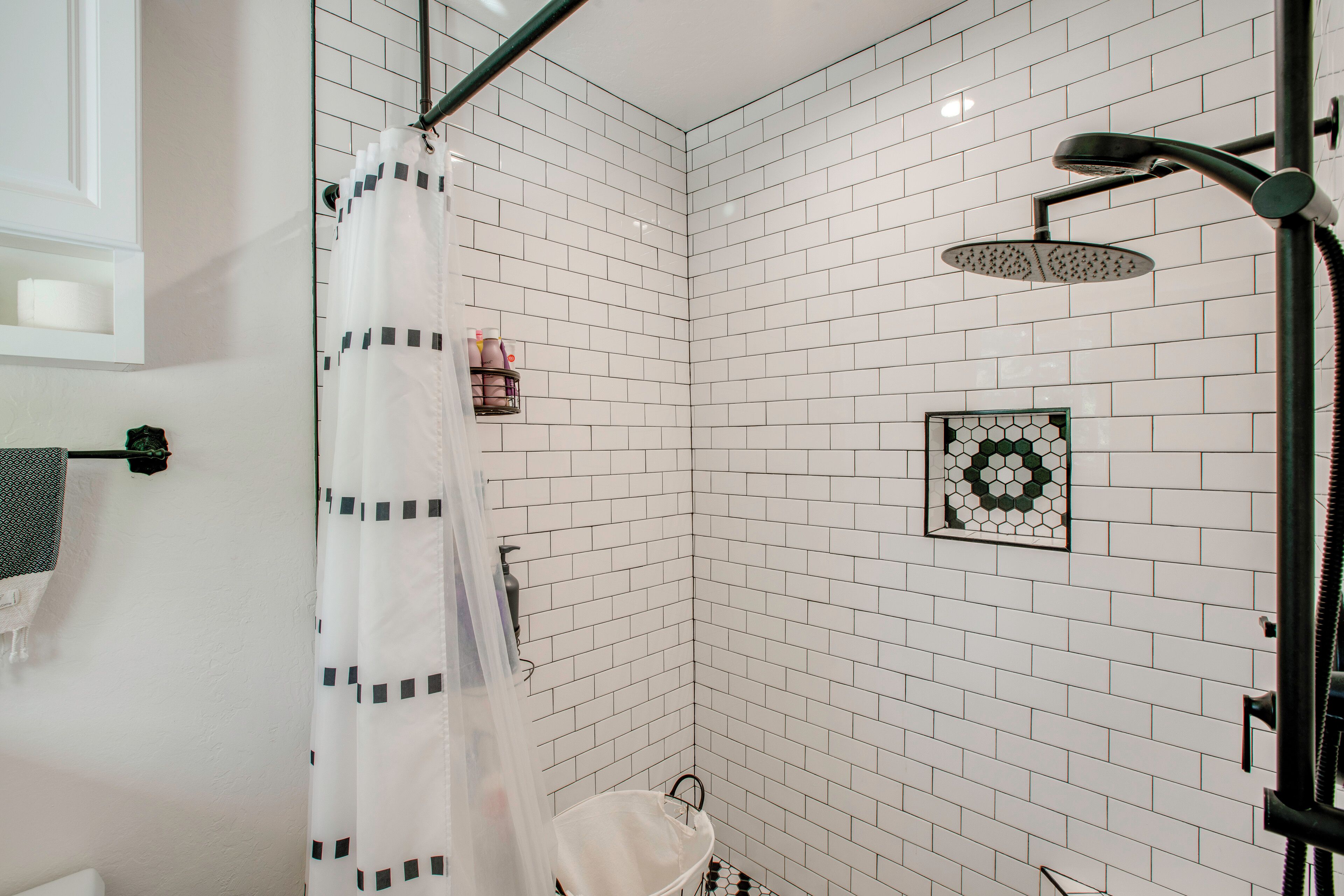 A corner shower with white tiled walls, a showerhead, and a hanging shower curtain.
