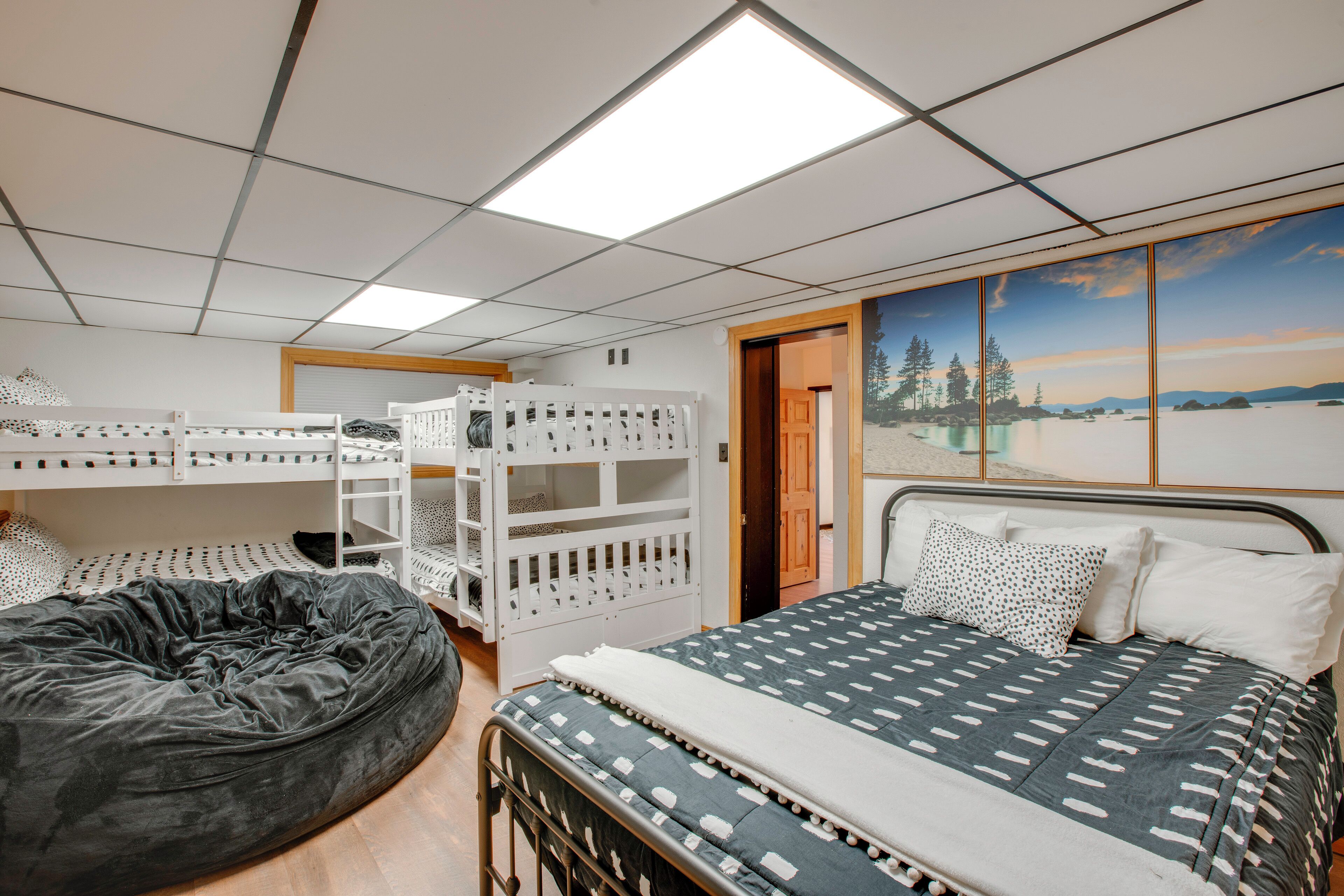 A room with bunk beds, a bean bag, a bed with patterned bedding, and a large window with a scenic view.